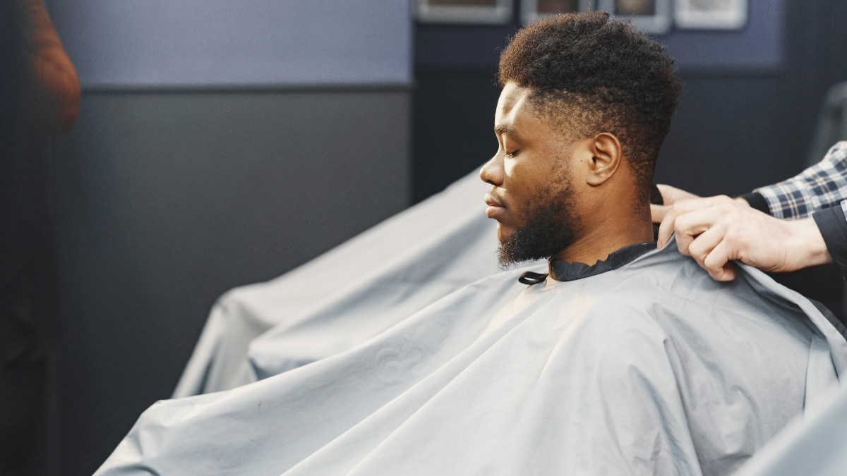 A client sits in his comfy barber chair, one of the must-have barbering products, as he gets his hair cut.