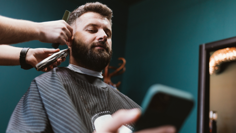 A barber works on his client's hair while in the chair as he examines the barbershop's digital marketing strategy.