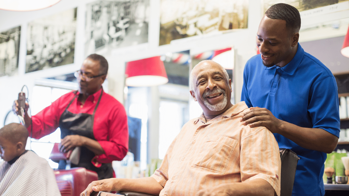 A client smiles while he gets his hair cut by his barber, a pro who has built a barbershop clientele community.
